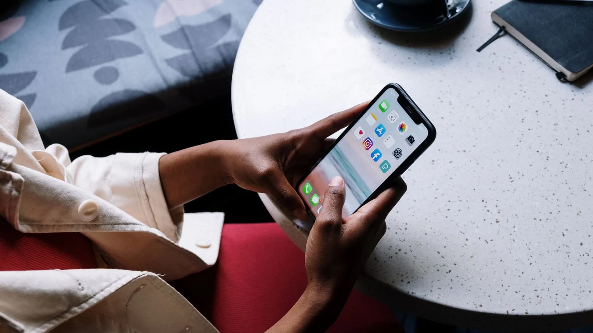 A person checks social media apps on a smartphone while sitting at a café table.