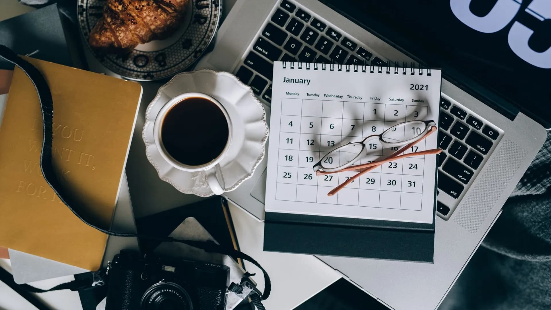 A serene workspace setup with coffee, croissant, laptop, and calendar, ideal for organizing plans.