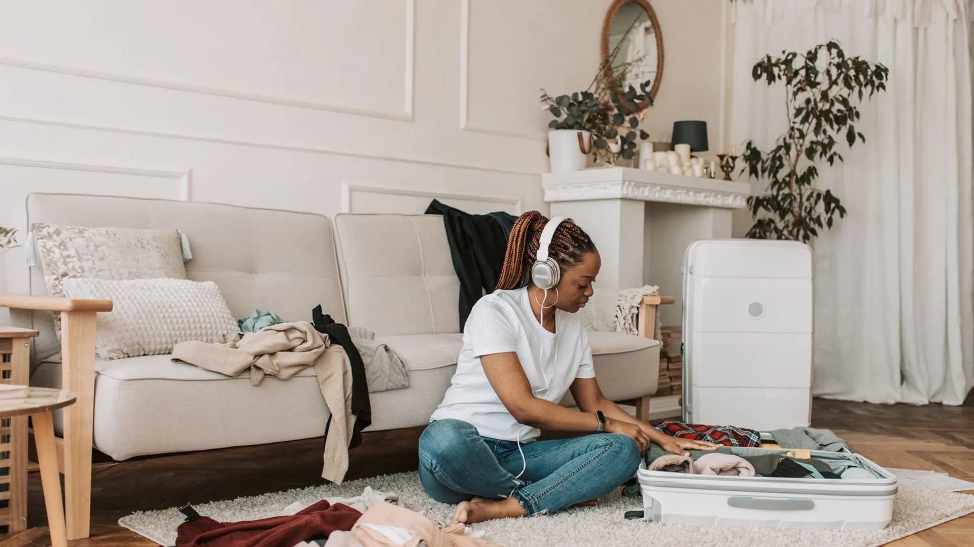 A woman with headphones packing a suitcase in her stylish living room, preparing for travel.
