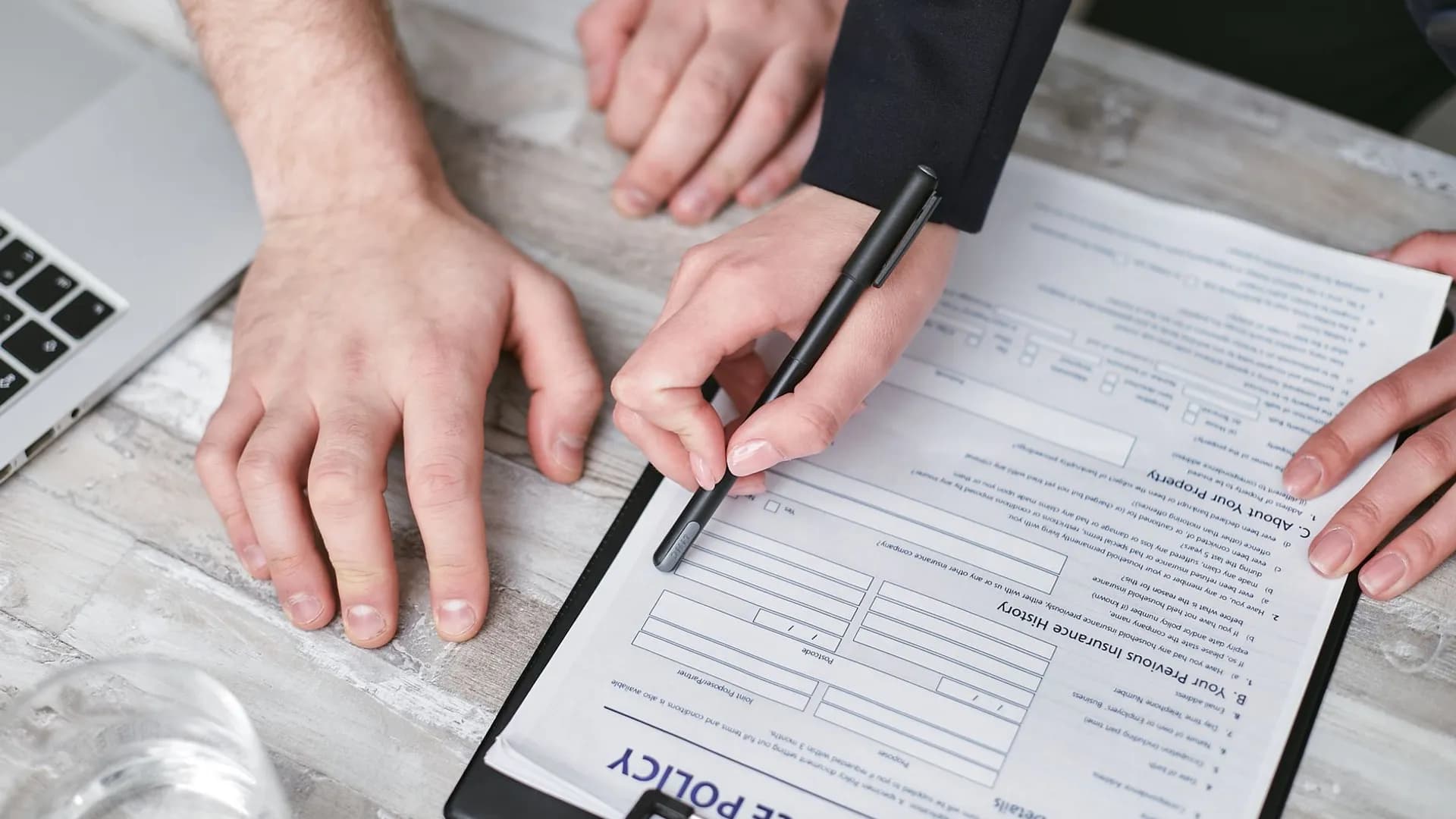 Close-up image of two people signing an insurance policy document on a wooden desk.