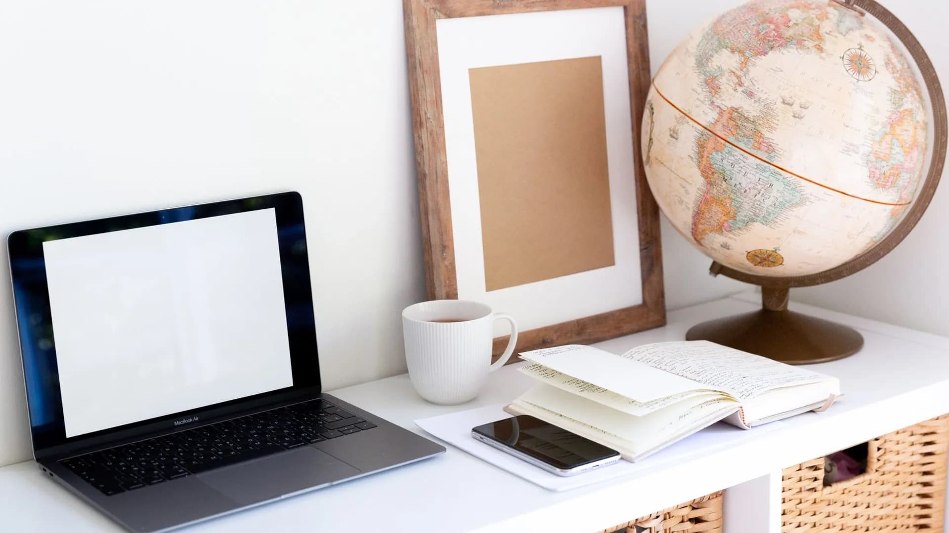 Laptop with empty screen placed near smartphone and organizer with blank frame and retro glove aside during coffee break in room