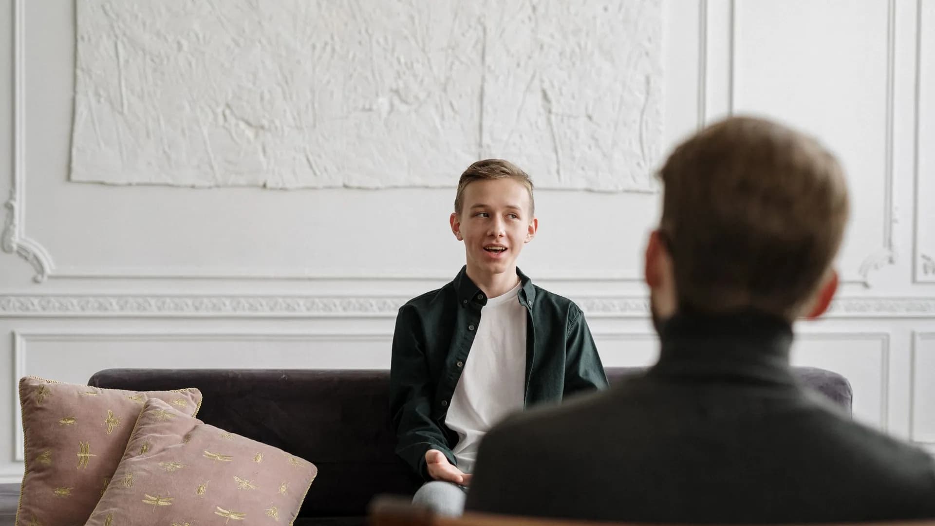 A young man engages in a therapy session with a counselor in a modern office setting.