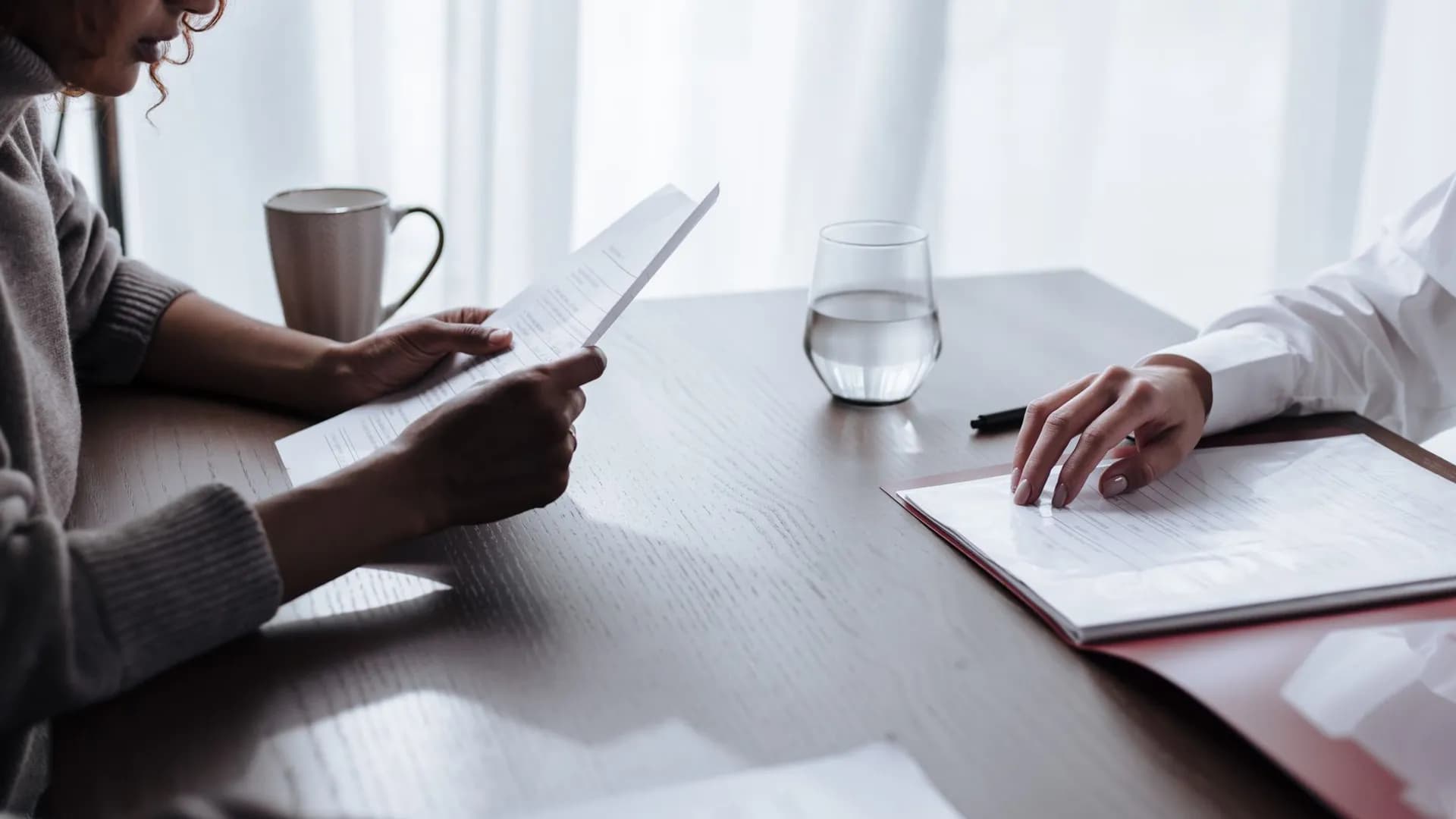 Two women reviewing documents with coffee and water on a table.