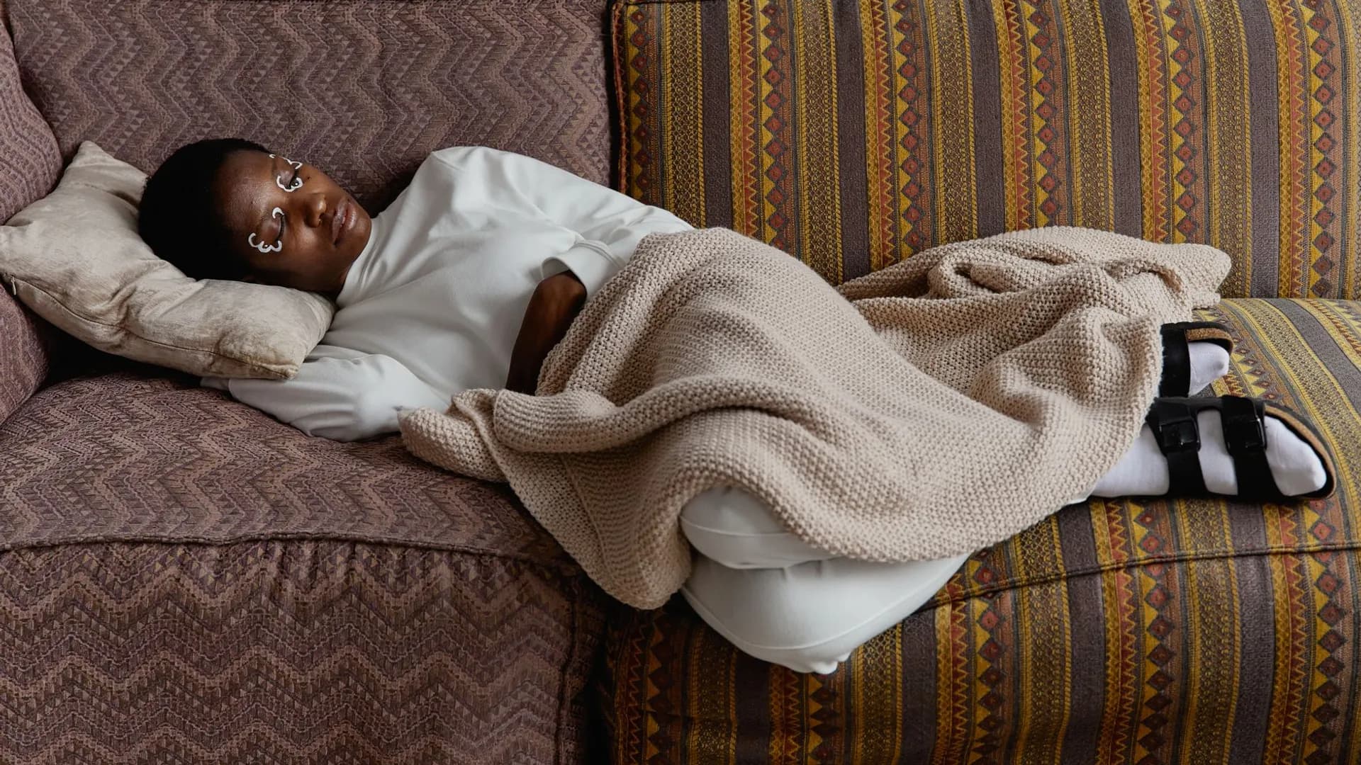 Fashionable young woman with face paint relaxing indoors on a cozy couch with blankets.