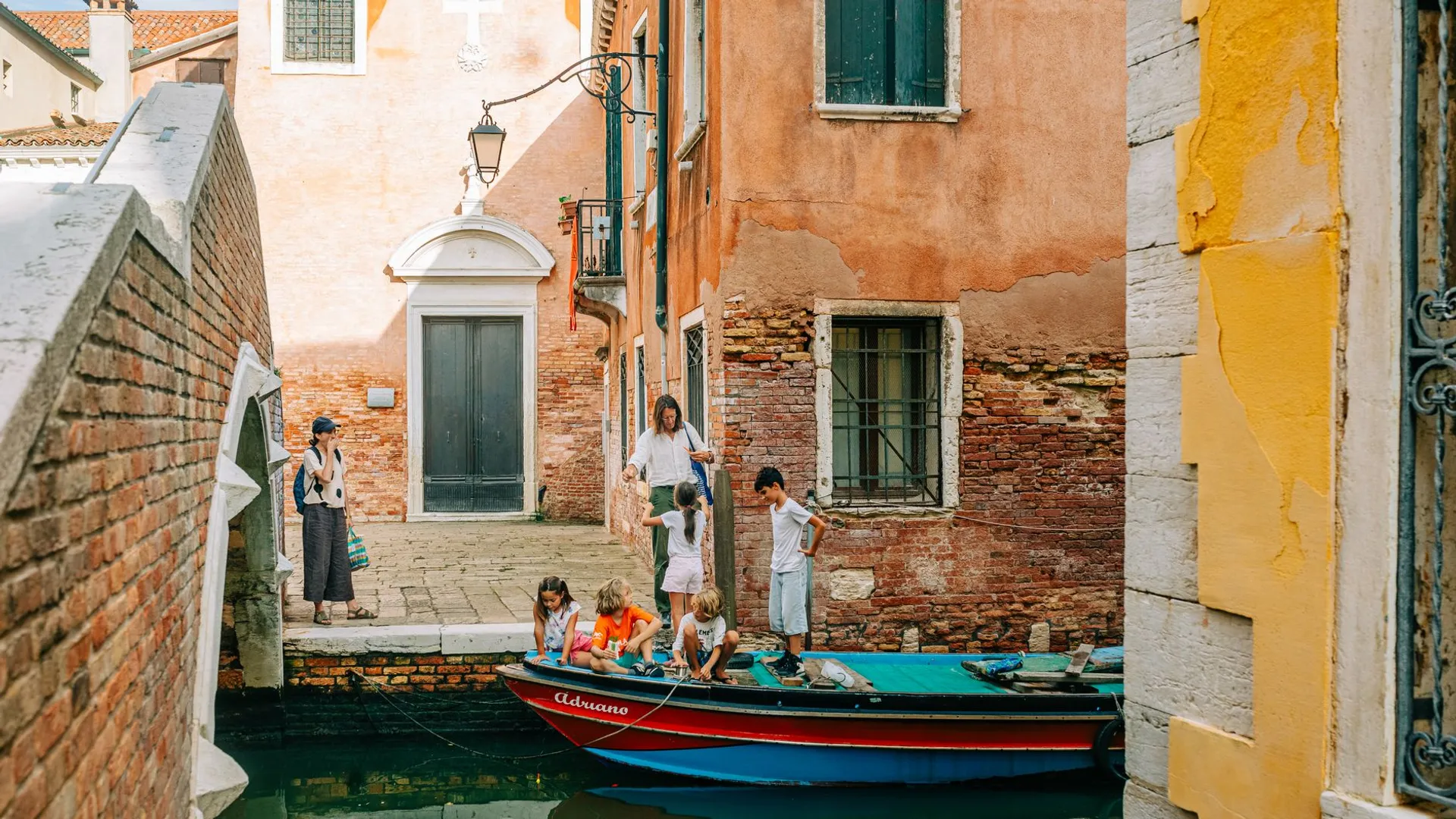 Charming scene of people by a canal in Venice, featuring historic architecture and a boat.