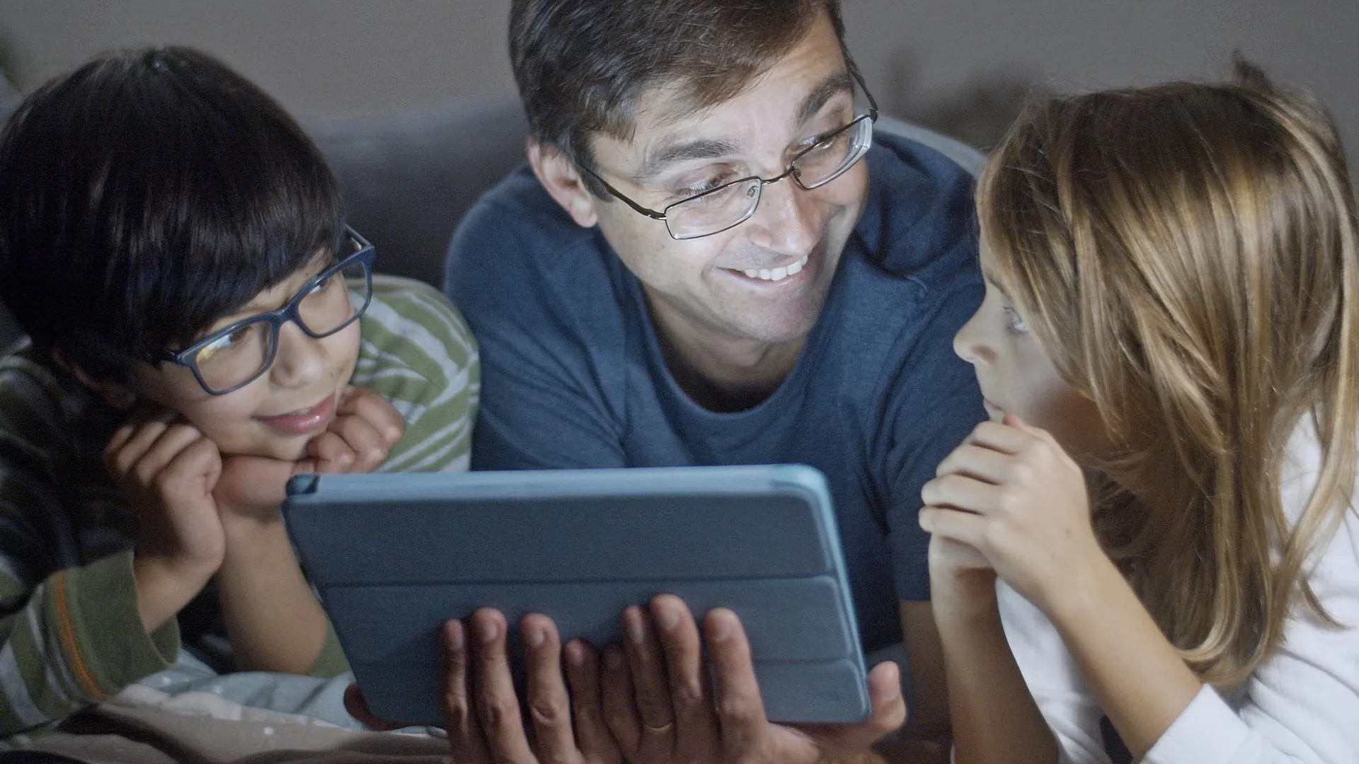 A father and two kids happily watching a tablet together, creating family bonding moments.