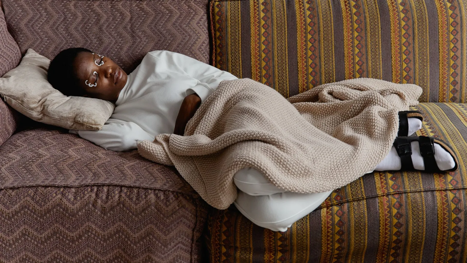 Fashionable young woman with face paint relaxing indoors on a cozy couch with blankets.
