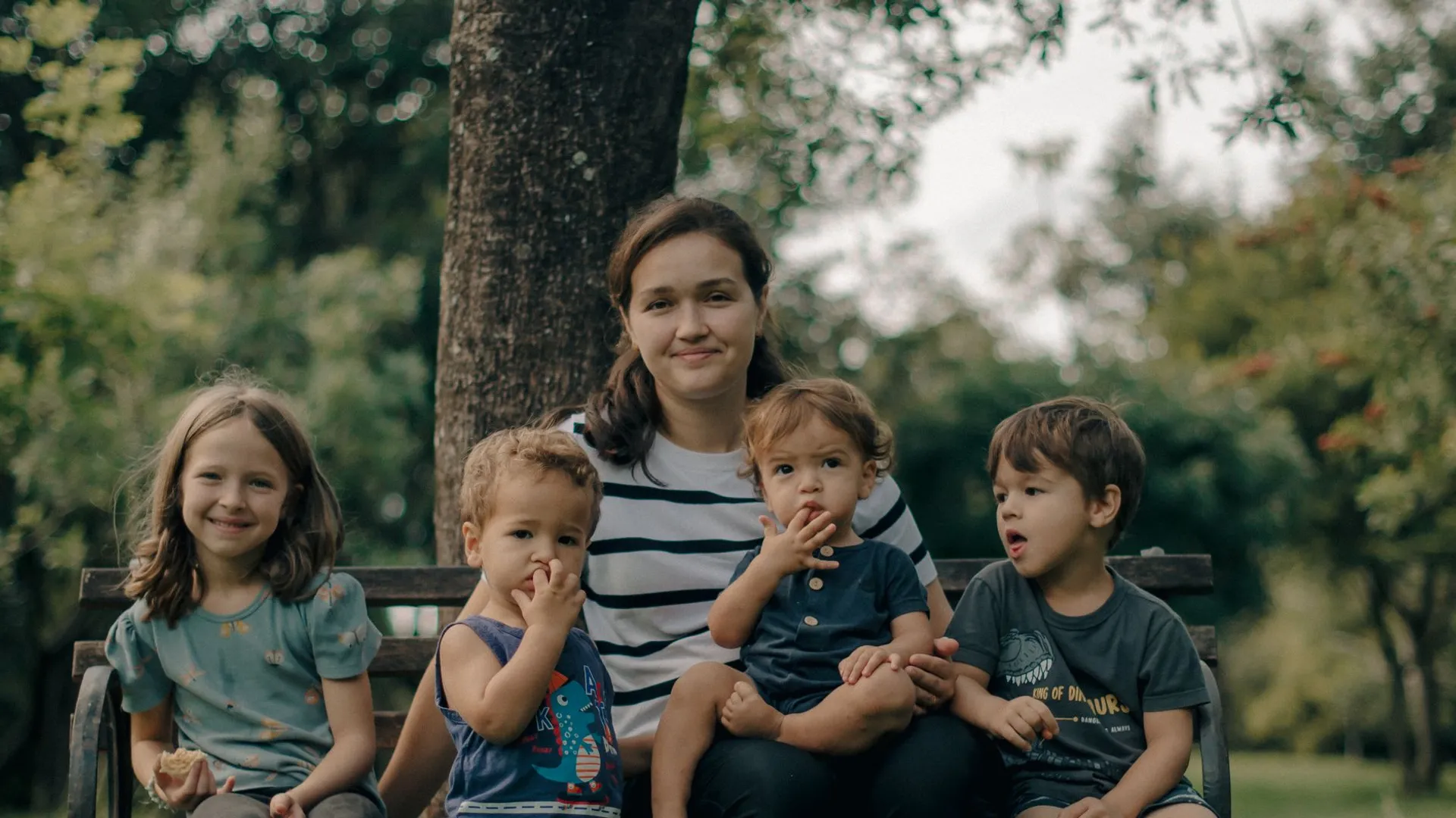 A mother with four children relaxing in a lush, green outdoor park setting.